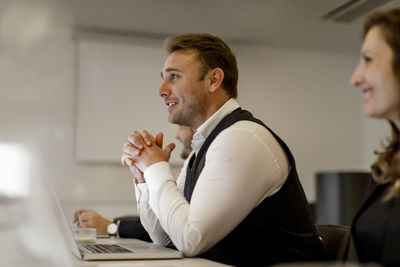 Smiling businessman with hands clasped discussing in meeting at office