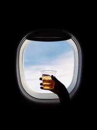 Cropped hand of person holding drink by airplane window