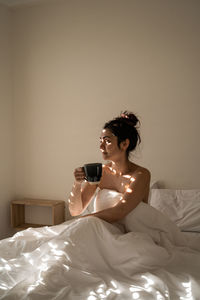 Young woman drinking glass on bed