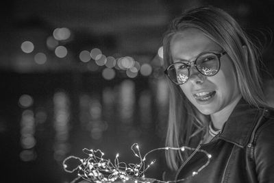 Close-up young woman holding illuminated string light at night