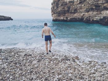 Rear view of shirtless man standing at beach