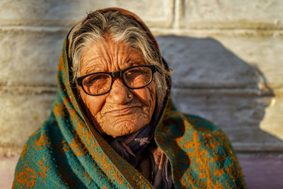 Close up portrait of a old aged woman sitting with the support of the wall in the sunset