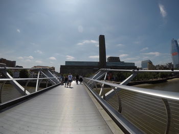 People walking on footbridge in city against sky