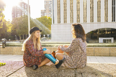 Young woman with prosthetic leg sitting with female friend on footpath in city
