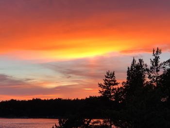 Silhouette trees by lake against romantic sky at sunset