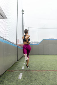 Full body of enduring female athlete in activewear running above ground during intense training in stadium