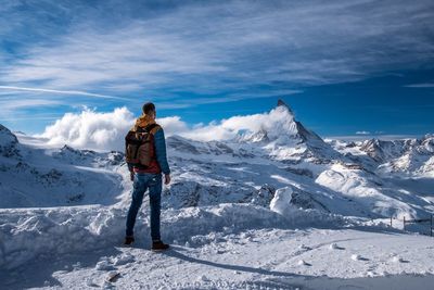 Rear view of mid adult man with backpack standing on snow against sky