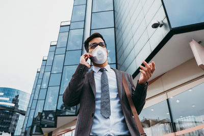 Business man with protective face mask using phone on city street.