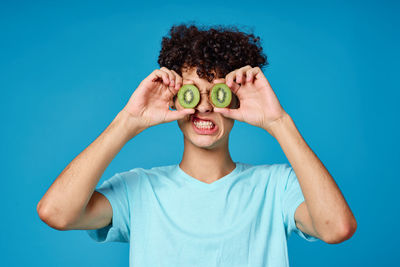 Portrait of man holding kiwi slices standing against blue wall