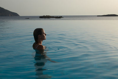 Woman in infinity pool by sea during sunset