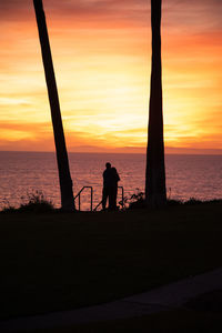 Silhouette men standing on beach against orange sky