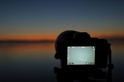 Close-up of camera against sky during sunset