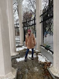 Full length of woman standing in snow by railing during winter