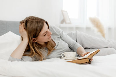 Young girl reading a book while lying on bed at home