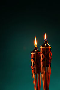 Close-up of illuminated tiki torches against green background