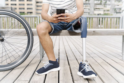 Low section of man with artificial limb using mobile phone in city