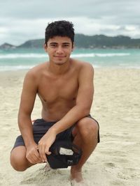 Portrait of young man crouching on sand at beach