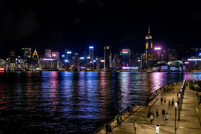 Illuminated buildings by river against sky at night