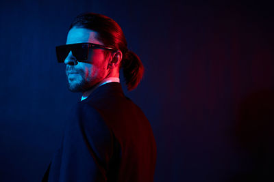 Young man wearing sunglasses while standing against black background