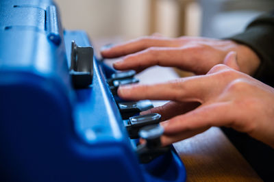 Crop anonymous visually impaired male typing on typewriter with tactile writing system at home