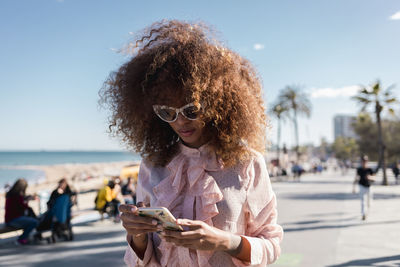 Young woman using mobile phone against sky