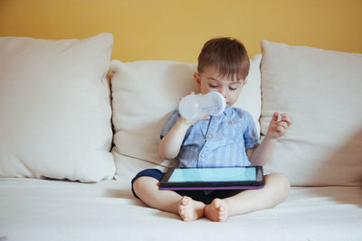 Rear view of boy using mobile phone while sitting on sofa