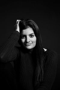 Portrait of smiling young woman with long hair standing against black background