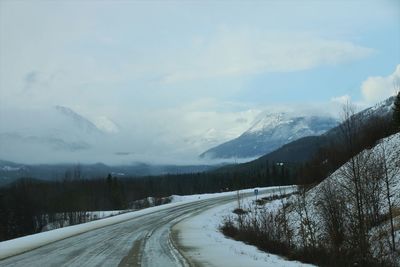 Empty road amidst snow covered mountains against sky