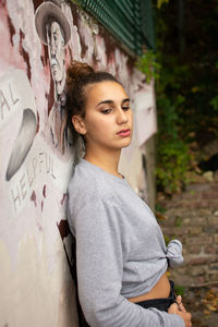 Portrait of young woman standing against graffiti wall