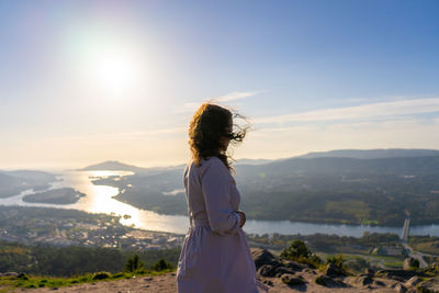 Side view of woman looking at landscape against sky during sunset