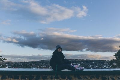 Portrait of woman sitting on wall against sky