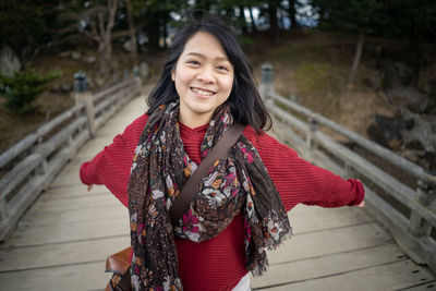 Portrait of smiling young woman with arms outstretched standing on boardwalk