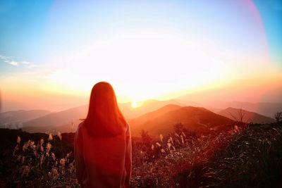 Rear view of woman standing on field against sky during sunset