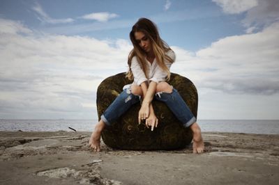 Young woman sitting on beach against sky