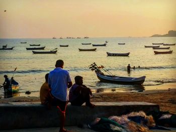 Rear view of people on beach against sky during sunset