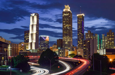 Light trails on road amidst buildings against sky at night