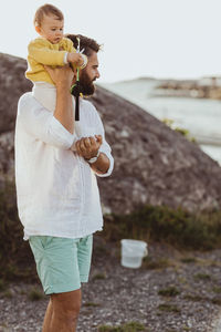 Father carrying daughter on shoulder while standing on rock formation