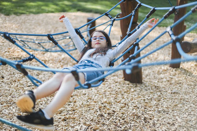 Caucasian girl lying down rides on a rope swing in the park at the playground