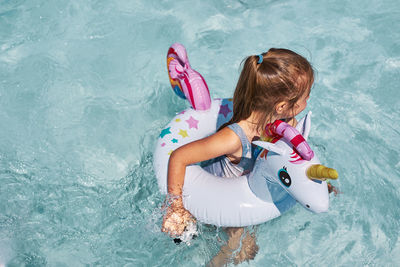 Little girl playing in a swimming pool with inflatable rubber ring toy in the shape of unicorn