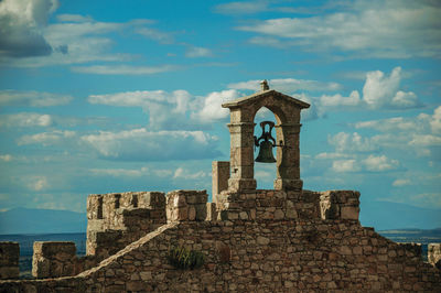Bell on top of thick stone wall with crenels and merlons at the castle of trujillo. spain.