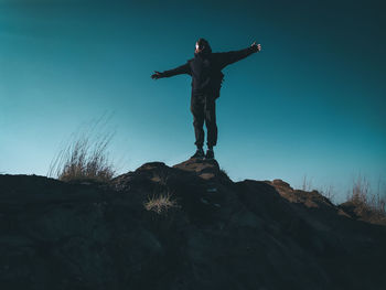 Low angle view of man standing on rock against sky