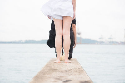 Low section of people on pier over sea against sky