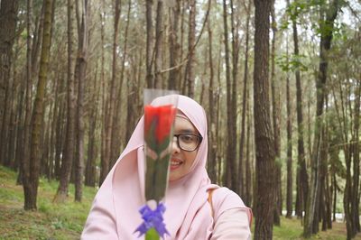 Portrait of young woman holding flower in forest