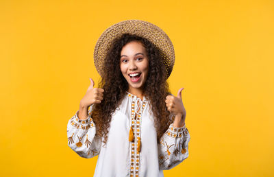 Portrait of young woman standing against yellow background