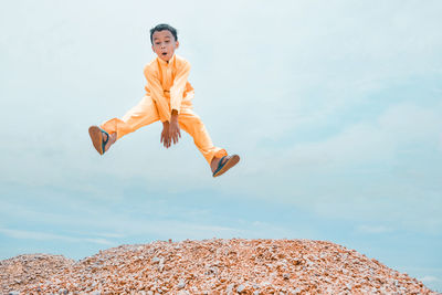 Playful boy jumping on rocks against cloudy sky