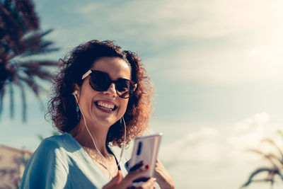Portrait of happy young woman using mobile phone against sky