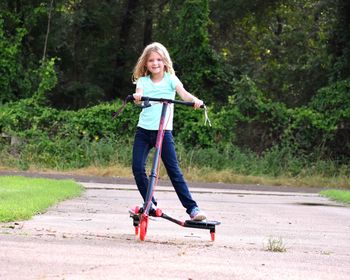 Full length portrait of happy boy riding skateboarding on road