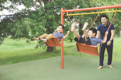 Father with sons enjoying swings at park