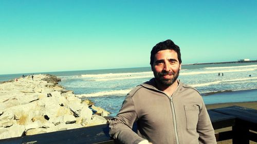 Portrait of smiling man standing at beach against clear sky