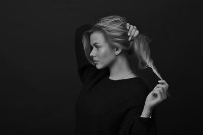 Portrait of young woman standing against black background